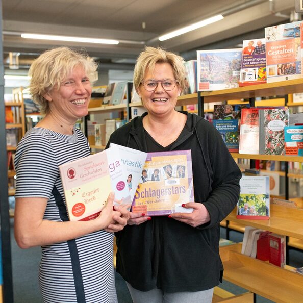 Die Leiterin der Hürther Stadtbücherei Barbara Hoevels (links im Bild) und ihre Mitarbeiterin Sabine Wingen präsentieren einen Teil der gespendeten Produkte.