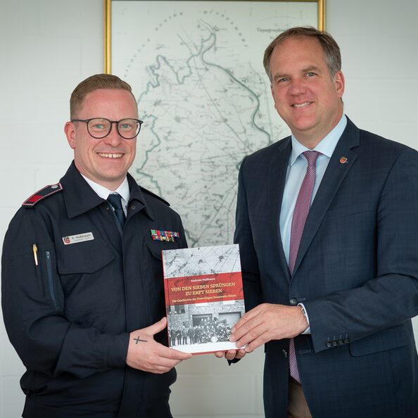 Feuerwehrmann Andreas Nußbaum überreicht sein neues Buch mit dem Titel „Von den sieben Sprüngen zu Erft sieben“ an Bürgermeister Dirk Breuer.